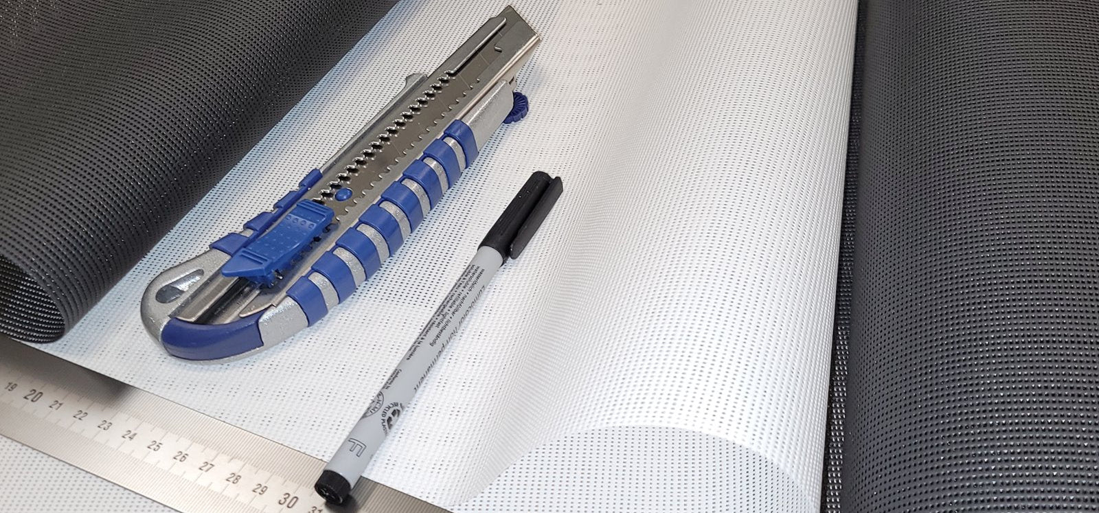 Sonnenschutzstoff mit Cuttermesser und Stift.